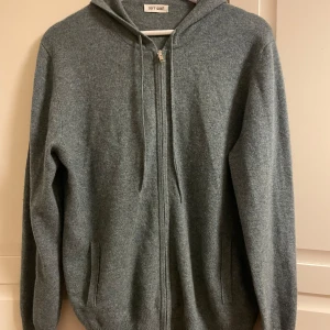 Cashmere hoodie från Soft Goat - Säljer en stilren och aldrig använd grå/grön cashmere hoodie från Soft Goat. Den är storlek medium. Tröjan har dragkedja framtill och en praktisk huva med snörning. Perfekt för kyliga dagar.