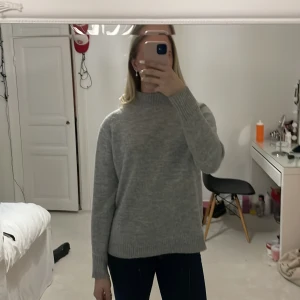 Grå stickad polotröja - Säljer en mysig grå stickad polotröja med långa ärmar. Perfekt för kyliga dagar och enkel att matcha med olika outfits. Tröjan har en klassisk design med ribbade kanter vid ärmslut och nederkant.