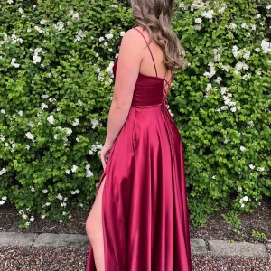 Vinröd långklänning från Fiesta Fashion - !!!!!PRIS KAN DISKUTERAS VID TILLFÄLLE!!!!Säljer en elegant vinröd balklänning från Fiesta Fashion köpt i en balklännings butik. Klänningen har smala axelband och en v-ringad design med snörning i ryggen. Tillverkad i ett glänsande siden material med en slits som ger en extra touch. Perfekt för student bal.  Pris kan diskuteras!