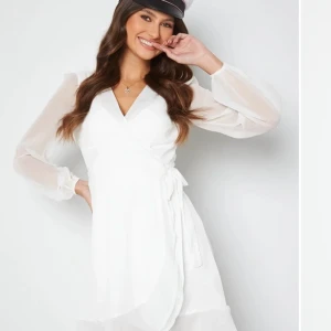 Vit omlottklänning - Snygg vit omlottklänning med långa ärmar och v-ringad design. Perfekt för en stilren look med knytning i midjan som ger en fin passform. Klänningen har en elegant och luftig känsla.