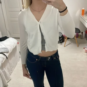 Vit kofta med knappar - Säljer en stilren vit kofta med knappar framtill. Den har en v-ringad design och långa ärmar, perfekt för en enkel och klassisk look. Passar bra till både jeans och kjol.