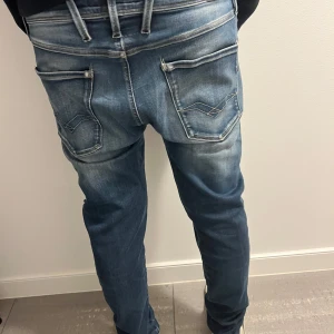 Replay Anbass Jeans - Snygga blå jeans från Replay med slitna detaljer och en modern look. De har en slim passform och är perfekta för en avslappnad stil. Jeansen har dragkedja och knappar samt klassiska fem fickor. skick 9,3/10