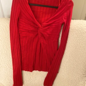 Röd ribbad topp - Snygg röd ribbad topp med v-ringning och knutdetalj framtill. Den har långa ärmar och är perfekt för en stilren look. Passar bra till både jeans och kjol.