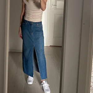 Blå jeanskjol från Stradivarius - Säljer en snygg blå jeanskjol från Stradivarius. Kjolen har en klassisk design med en rak passform och en diskret slits framtill. Perfekt för en avslappnad stil. 🦋