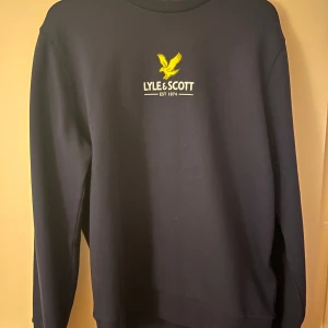 Svart tröja från Lyle & Scott - Säljer en stilren svart tröja från Lyle & Scott med deras ikoniska gula logga på bröstet. Tröjan har långa ärmar och en klassisk passform. Perfekt för en avslappnad look. Skick 5 av 5