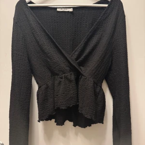 Svart omlottopp från NA-KD - Snygg svart omlottopp från NA-KD med långärmad design och volangdetaljer i midjan 💓