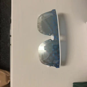 Blå solglasögon från Louis Vuitton - Snygga blå solglasögon från Louis Vuitton med ett unikt mönster på glasen. De har en modern design med en vit ram och blå detaljer. Perfekta för att ge din stil en lyxig touch./går pruta vid snabb affär