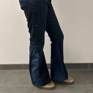 Svarta bootcut jeans med blå detaljer - Snygga svarta bootcut jeans med mörkblå bootcut. Perfekta för en unik stil med en klassisk twist. De har en mid/low  midja och är tillverkade i jeansmaterial.