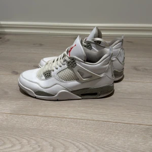  Nike Air Jordan 4  - Snygga vita Nike Air Jordans med grå och röda detaljer. Skorna har en klassisk design med snörning och synlig Air-dämpning i sulan. Perfekta för dig som vill ha en stilren look med en sportig touch. Den är använd nåra gånger och är på bra skick skulle inte säga nyskick