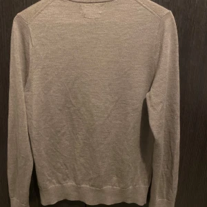 Beige merinoulltröja från Riley - Säljer en stilren beige tröja från Riley i mjuk merinoull. Tröjan har en klassisk rund hals och långa ärmar, perfekt för kyligare dagar. Passar både till vardags och mer uppklädda tillfällen.