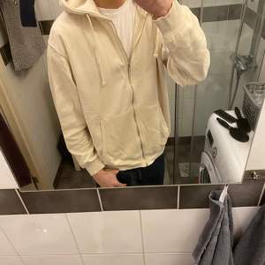 Säljer en beige hoodie med dragkedja och huva. Tröjan har långa ärmar och en klassisk passform. Perfekt för en avslappnad stil.