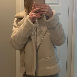 Beige jacka från stradivarius  - Säljer en snygg beige jacka från stradivarius med dragkedja och mjukt foder. Jackan har en pälskrage och muddar, vilket ger en lyxig känsla. Perfekt för kyligare dagar!