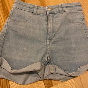 Högmidjade jeansshorts - Snygga ljusblå jeansshorts med klassisk femficksdesign och uppvikta benslut. Shortsen har en hög midja och är i fint skick! Strl 134