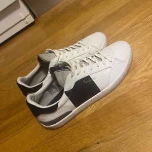 Pepe Jeans sneakers - Snygga vita sneakers med mörkblå detaljer och snörning. Skorna har en stilren design med en präglad text '1973' på hälen. Perfekta för en casual look. Påminner om Valentinos. nypris 1250