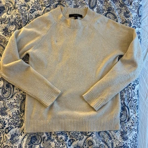Beige stickad tröja från Vero Moda - Säljer en stilren beige/vit stickad tröja från Vero Moda. Tröjan har långa ärmar och ribbade kanter vid hals, ärmslut och nederkant. 