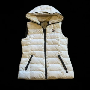 Moncler väst - En moncler väst med zip hela vägen upp.  Skavanker på kedjan i mitten har liten skada för själva hållaren har låsnat (sida 5). Och kjedjan på ena fickan är även skadad för att den är borta (sida 4) säljer billigt för osäker på äktighet. Storlek 4 men vet ej vad det är. Skulle säga storlek small