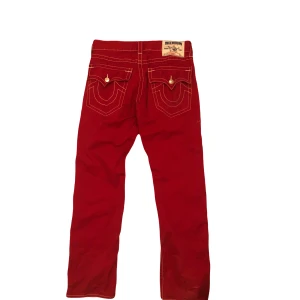 Röda jeans från True Religion - Snygga röda jeans från True Religion med kontrasterande vita sömmar.                                 Storlek:33 Benlängd:108 Midja:42 Gylf:26 Fotöppning:21 Lår:27 