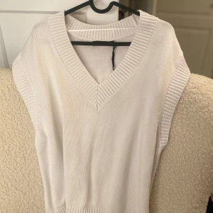 Vit stickad väst från Bik Bok - Säljer en stilren vit stickad väst från Bik Bok. Västen har en v-ringad design och ribbade kanter som ger en snygg och modern look. Perfekt för lager-på-lager-stil!