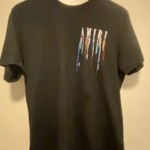 T shirt Amiri - Snygg svart t-shirt från Amiri med ett coolt färgglatt tryck som ser ut som rinnande färg både fram och bak. Perfekt för en stilren och modern look.