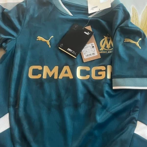  fotbollströja Marseille Wahi  - Snygg blå fotbollströja från Puma med guldiga detaljer och logotyp. Tröjan är helt ny. Lappen är kvar och har aldrig använt då den va för liten för mig. 