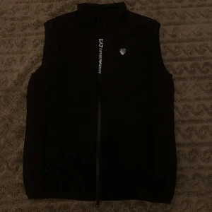 Emporio Armani EA7 Väst - Produkt: Väst från Emporio Armani Storlek: S Märke: Emporio Armani Färg: Svart ⚫️ Skick: Väldigt Bra  Beskrivning: En snygg väst i svart från Emporio Armani. Perfekt för vardagsbruk. I väldigt bra skick, inga större skador, knappast tecken på användning.   Frakt 🚚: Skickas inom 1-2 arbetsdagar efter betalning. Jag skickar via Postnord. Paketet är spårbart! 📨 
