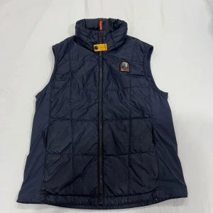 Mörkblå  väst från Parajumpers - Säljer en snygg mörkblå quiltad väst från Parajumpers med dragkedja och hög krage. Västen har en broderad logga på bröstet och orange detaljer på insidan. Perfekt för kyliga dagar!