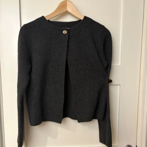 Mörkgrå kofta från Zara - Säljer en stilren mörkgrå kofta från Zara. Koftan har en enkel knapp framtill och är tillverkad i ett mjukt material som passar perfekt för kyligare dagar. Den har långa ärmar och en klassisk design som gör den lätt att matcha med olika outfits.