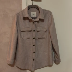 Beige overshirt från Object - Snygg beige overshirt från Object med knappar framtill och två bröstfickor. Perfekt för lager-på-lager-stil. Den har en klassisk krage och långa ärmar.