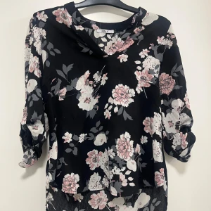 Svart blommig blus från Hollis - Säljer en elegant svart blus från Hollis med vackert blommönster i rosa och vitt. Blusen har trekvartsärmar och en avslappnad passform. Perfekt för att ge en stilfull touch till din garderob.Skriv för fler bilder eller om ni har fler frågor 💓