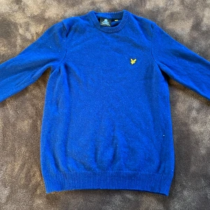  Lyle & Scott - Säljer en snygg blå tröja från Lyle & Scott med deras ikoniska gula logga på bröstet. Tröjan är långärmad och tillverkad i ett mjukt material som passar perfekt för kyligare dagar. 