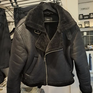 Svart jacka från Bikbok - Snygg svart jacka från Bikbok med pälskrage och dragkedja. Jackan har en cool bikerstil med bälte vid kragen och är perfekt för kyligare dagar. Den är fodrad med mjukt material för extra värme och komfort. Jätte mjuk och skön. Ej använd mycket så nyskick. Lite oversize modell.