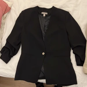 Svart kavaj med knapp - Snygg svart kavaj med en enkel knapp framtill. Den har en klassisk design med 3/4 långa ärmar och en stilren look. Perfekt för en elegant och professionell stil. Lika snygg till ett par slitna jeans som till pennkjolen! 