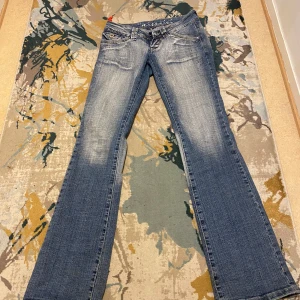 Blå bootcut jeans från Miss Sixty - Snygga blå bootcut jeans från Miss Sixty med en cool slitningseffekt. De har klassisk femficksdesign och en knappgylf. Perfekta för en avslappnad stil med en touch av retro. Där de är från 2009 knappt använt 