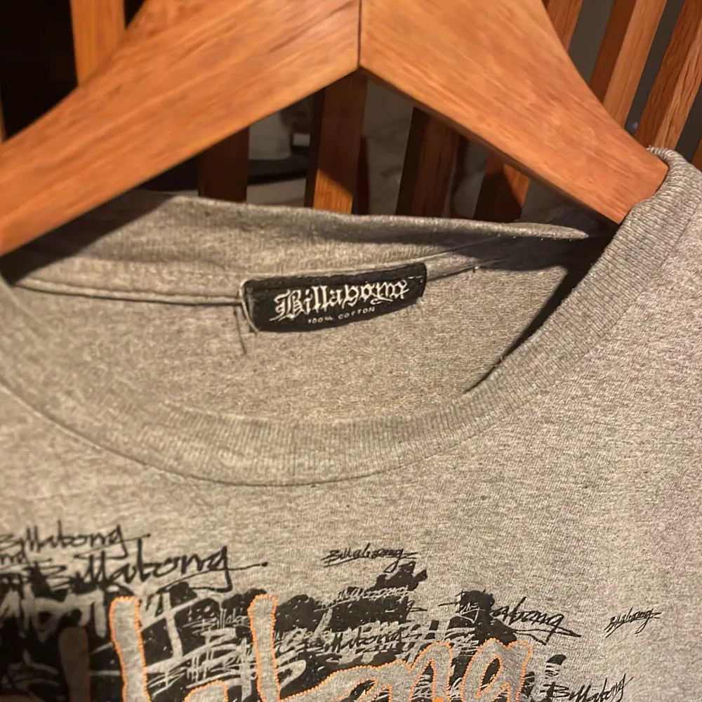 Säljer en grå t-shirt från Billabong med ett coolt tryck i svart och orange på framsidan. T-shirten är kortärmad och gjord av bomull, perfekt för en avslappnad stil. Passar bra till jeans eller shorts!. T-paidat.