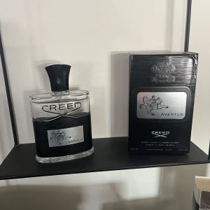 Creed Aventus Parfym - Exklusiv Creed Aventus parfym i en elegant glasflaska med svart kork. Förpackningen är stilren och svart med silverdetaljer. En doft som utstrålar lyx och elegans, perfekt för den som vill sticka ut.