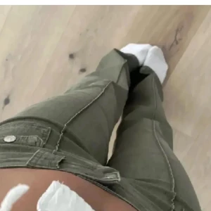 Olivgröna byxor med fickdetaljer - Säljer ett par olivgröna byxor i mycket bra skick. De har en tight passform och är lågmidjade med snygga fickdetaljer och knappar framtill. Perfekta för höst och vår, och kan stylas både upp och ner beroende på tillfälle. Första två bilder är lånade