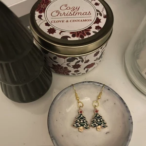 Julgransörhängen i guld och grönt - Superfina örhängen formade som julgranar med gröna detaljer och små röda stjärnor på toppen. De har en guldig krok och är perfekta för att sprida julstämning. Passar perfekt till julens alla festligheter! 🎄✨