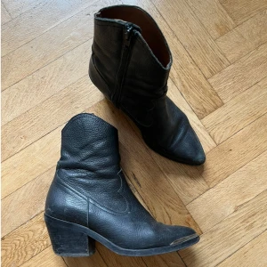 Svarta boots med dragkedja - Säljer ett par svarta boots i skinn med dragkedja på sidan. De har en robust klack och en spetsig tå, vilket ger dem en cool och edgy look. Perfekta för höst och vinter, och funkar lika bra till vardags som till fest. De är i bra skick med lite slitage på tån, men det ger bara karaktär! Stl 38.