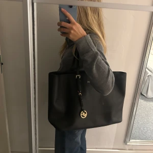 Svart axelväska från Michael Kors - Säljer en stilren svart axelväska från Michael Kors i mycket bra skick. Väskan är gjord av skinn och har en elegant design med gulddetaljer och en praktisk dragkedja. Många fack och innefickor. Använd fåtal gånger