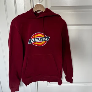 Vinröd hoodie från Dickies - Säljer en snygg röd hoodie från Dickies i storlek S. Den har en stor logga på framsidan och en praktisk magficka. Perfekt för höst och vinter, och den är i bra skick, använd Max 10 gånger.   Varan finns i Enköping och jag har möjlighet att mötas upp alternativt posta emot frakt!💞 Vid intresse kan flera detaljerade bilder skickas/ bilder med tröjan på! Tvättas innan den säljs/skickas! Pris går alltid att diskutera!