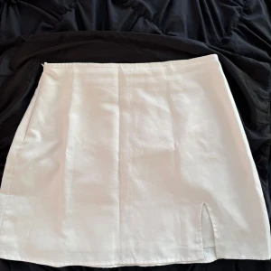 Vit kjol från Shein - Säljer en stilren vit kjol från Shein i storlek EU 40/42 Kjolen har en enkel design med en liten slits framtill som ger en snygg detalj. Perfekt för både vardag och festliga tillfällen. Materialet känns lätt och bekvämt.