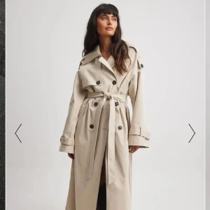 SÖKER NAKD Beige trenchcoat med bälte - Säljer en snygg beige trenchcoat i klassisk stil. Den har långa ärmar och ett bälte i midjan för en perfekt passform. Perfekt för höst och vår! 🧥