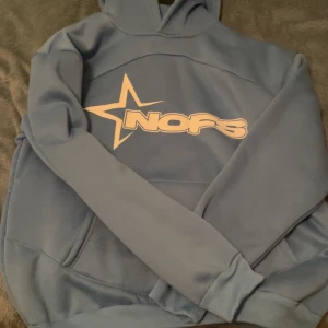 Blå hoodie med tryck - Säljer en snygg blå hoodie med ett coolt tryck på framsidan. Den är i bra skick och perfekt för höst och vinter. Hoodien har en normal passform och är gjord i mjukt material för extra komfort. Perfekt för vardagsbruk eller chillkvällar!