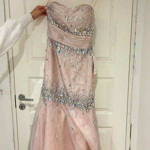 Rosa axelbandslös klänning med paljetter - Säljer en fantastisk rosa axelbandslös klänning med glittrande paljetter och pärlor. Den har en elegant passform och är perfekt för bal eller fest. Klänningen är i mycket bra skick och har en vacker, lång design som ger en lyxig känsla. 