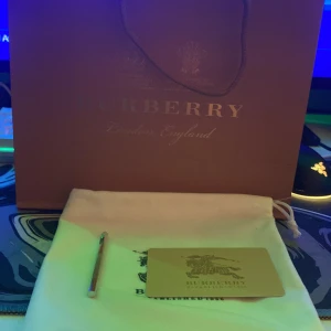 Rutig Burberry bälte - Säljer ett snyggt Burberry bälte i klassiskt rutigt mönster. Bältet har en stor metallspänne med Burberrys ikoniska logotyp. Perfekt för att ge en touch av lyx till vilken outfit som helst. Kommer med originalpåse och förpackning.