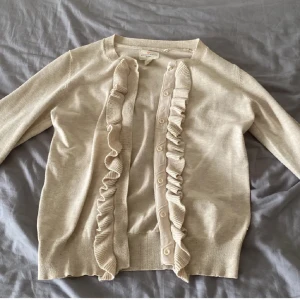 Beige kofta med volangdetaljer - Säljer en superfin beige kofta med volangdetaljer längs knäppningen. Perfekt för både vardag och fest! Den är i ett mjukt material och har långa ärmar. Passar perfekt till höst och vår. 