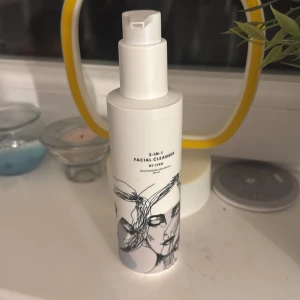 5-in-1 Facial Cleanser - En stilren flaska med en 5-i-1 ansiktsrengöring från Evo. Perfekt för en enkel och effektiv hudvårdsrutin. Flaskan har en modern design med en konstnärlig illustration på framsidan.