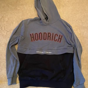 Grå och svart hoodie från Hoodrich - Säljer en snygg grå och svart hoodie från Hoodrich. Den har en stor logga på bröstet och texten 'FROM NOTHING TO SOMETHING' under. Perfekt för en casual look eller att chilla i. Den är i bra skick och superbekväm med en stor ficka fram. Passar perfekt till höst och vinter!