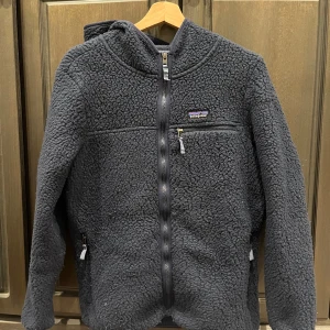 Mörkblå fleecejacka från Patagonia - Säljer en supermysig mörkblå fleecejacka från Patagonia i storlek L. Den har en dragkedja framtill och en praktisk huva. Perfekt för kyliga höst- och vinterdagar. Jackan är i bra skick och redo för nya äventyr! 💙