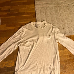 Vit långärmad tröja från Our Legacy - Säljer en stilren vit långärmad tröja från Our Legacy. Den har en praktisk bröstficka och är i ett mjukt bomullsmaterial. Perfekt för både vardag och lite finare tillfällen. Passar bra till jeans eller chinos!